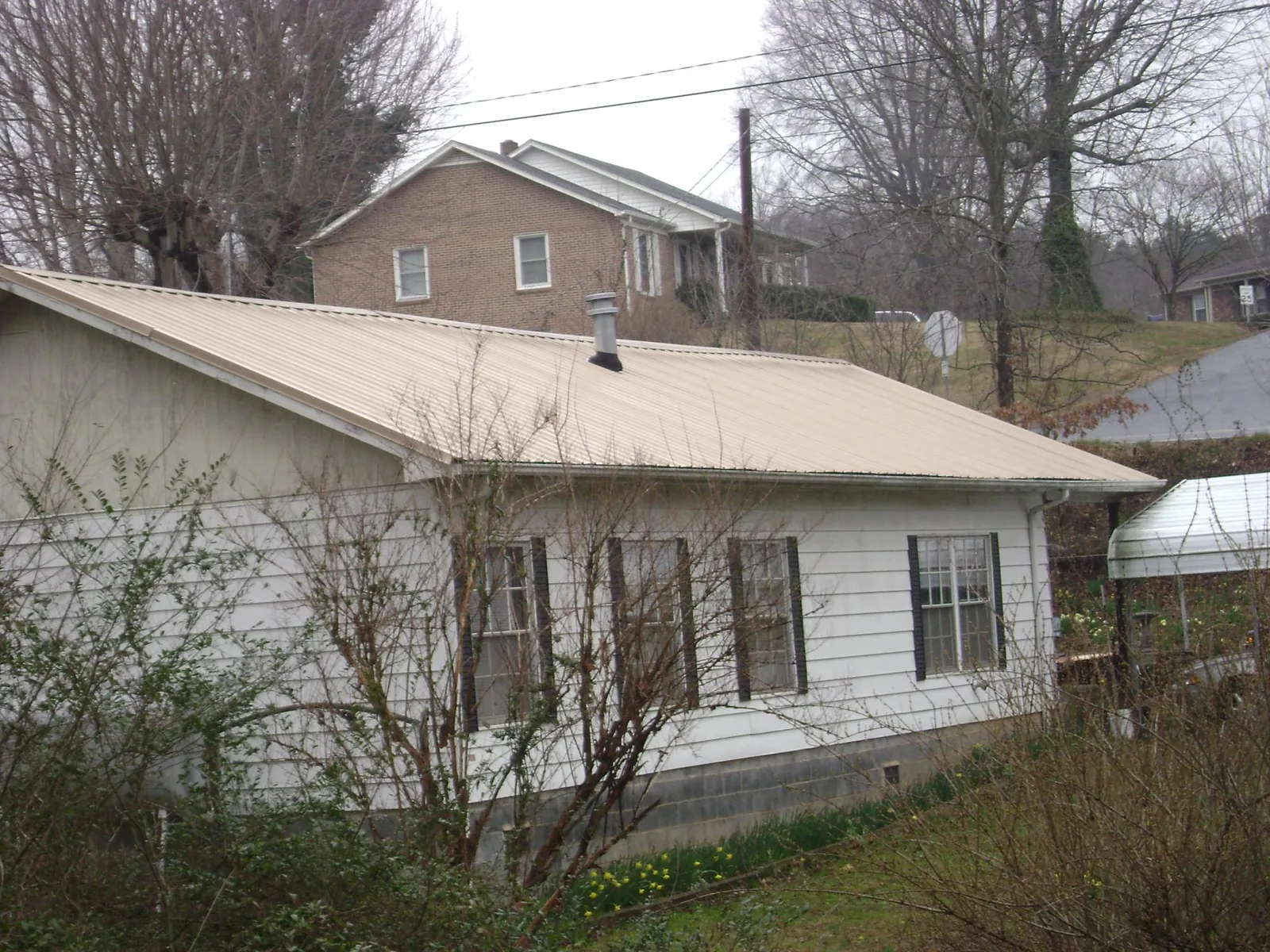 Tan metal roof on a white sided house set into a hillside — Commercial Roofing by Roofing Brothers in Kirkland